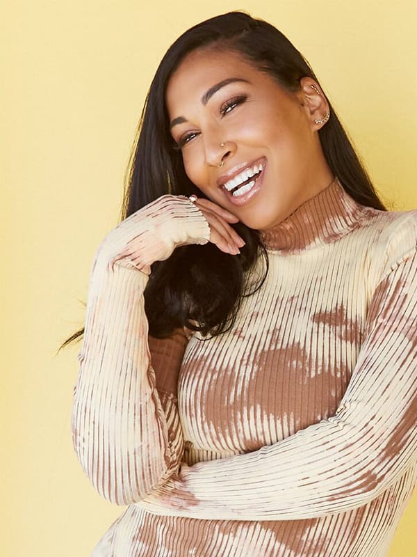 Woman in yellow background wearing beige ribbed sweater, smiling warmly.