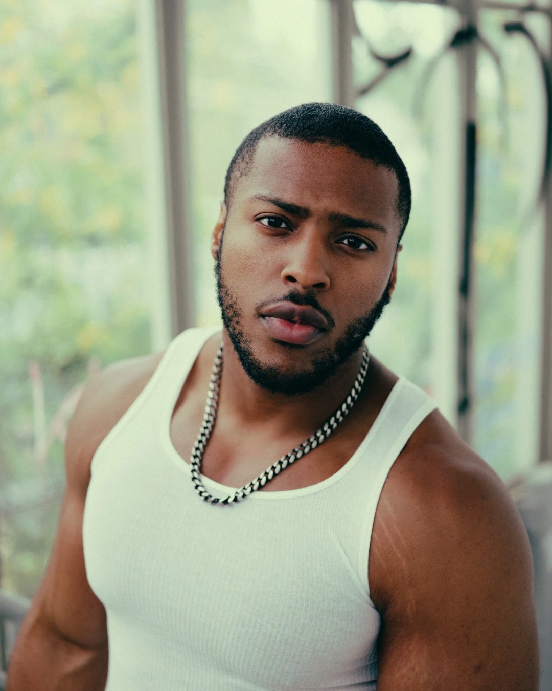 Unsighted Poet wearing a white tank top and chain